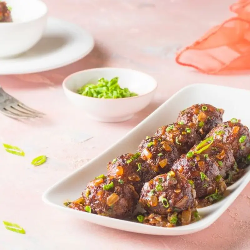 Vegetable balls made from a mix of finely chopped veggies, coated in a crispy batter and tossed in a tangy, spicy Manchurian sauce, Indo-Chinese favorite is garnished with spring onions.